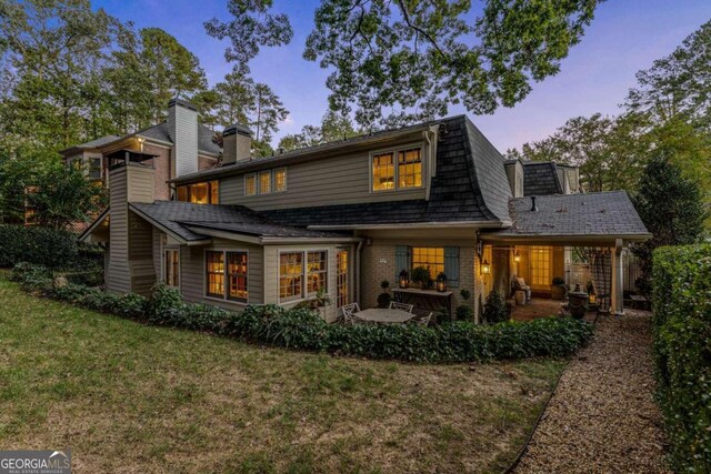 back house at dusk with a patio area and a lawn