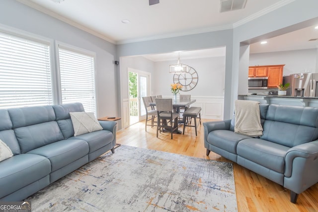 living room featuring a notable chandelier, ornamental molding, and light hardwood / wood-style flooring