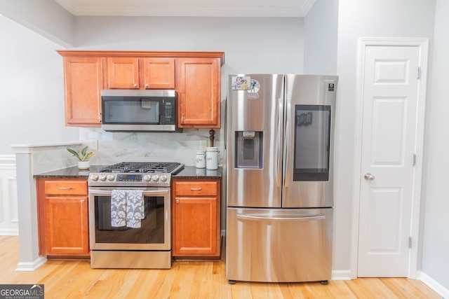 kitchen with ornamental molding, light hardwood / wood-style flooring, stainless steel appliances, and dark stone counters