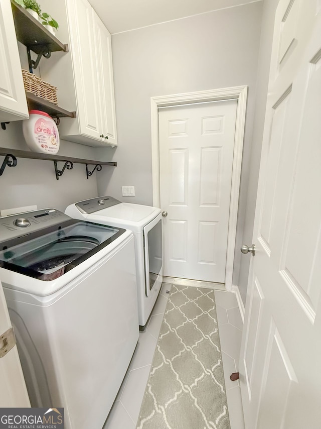 washroom with light tile patterned flooring, cabinets, and washer and clothes dryer