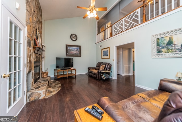 living room featuring dark hardwood / wood-style floors, high vaulted ceiling, ceiling fan, and a stone fireplace