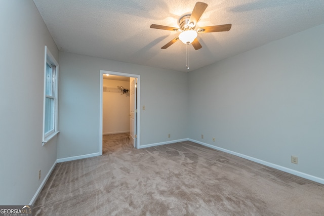 unfurnished bedroom featuring a spacious closet, a closet, ceiling fan, and light carpet