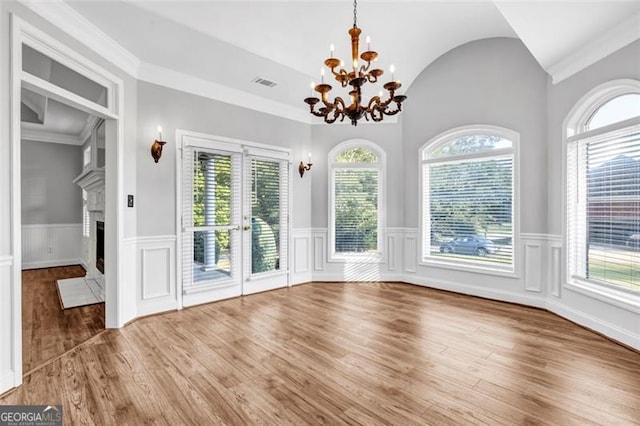 unfurnished dining area featuring vaulted ceiling, a chandelier, a fireplace, and wood-type flooring