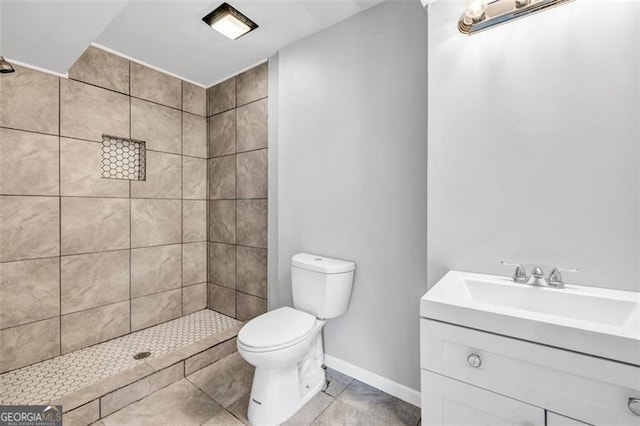 bathroom with vanity, toilet, a tile shower, and tile patterned flooring