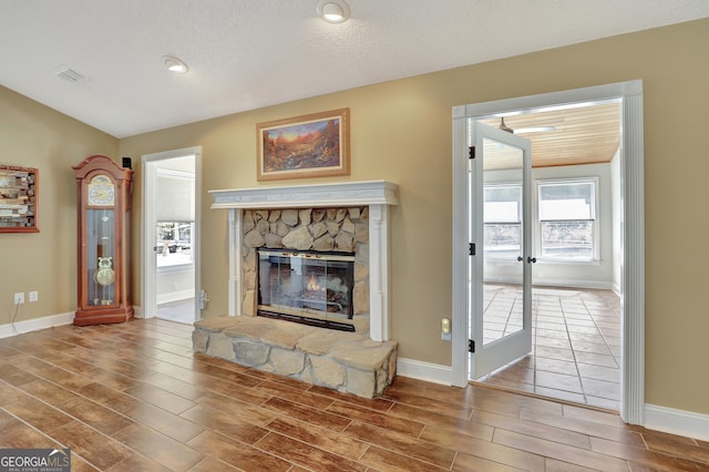 unfurnished living room featuring a stone fireplace, french doors, and a textured ceiling