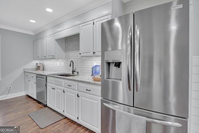 kitchen featuring appliances with stainless steel finishes, white cabinetry, sink, decorative backsplash, and light stone countertops