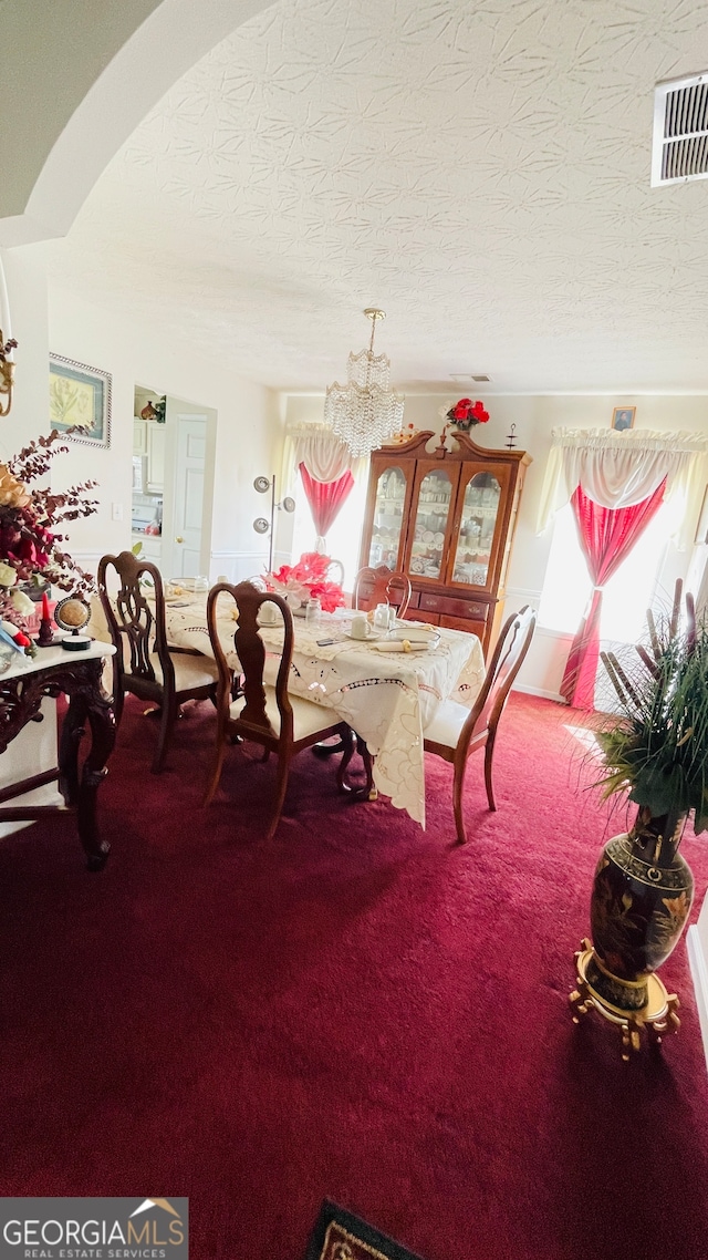 dining space featuring a notable chandelier, a healthy amount of sunlight, a textured ceiling, and carpet floors