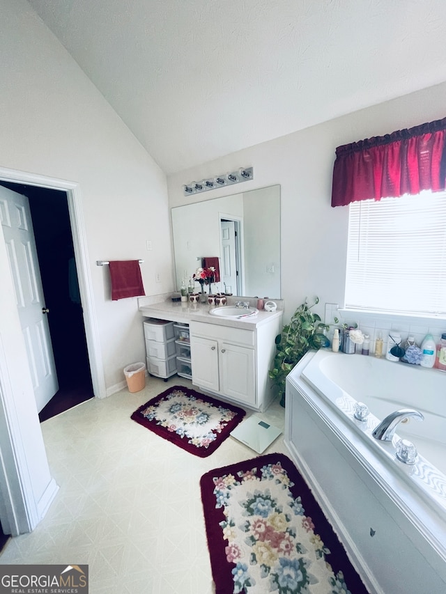 bathroom featuring vanity, vaulted ceiling, a textured ceiling, and a tub