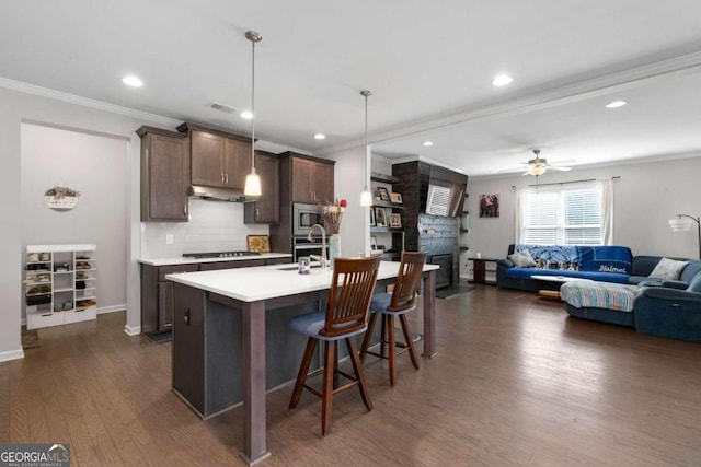 kitchen featuring appliances with stainless steel finishes, dark hardwood / wood-style flooring, pendant lighting, ornamental molding, and a center island with sink