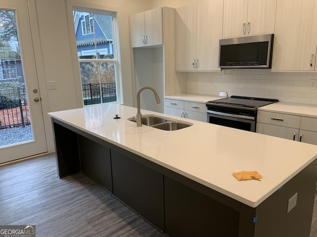 kitchen featuring hardwood / wood-style floors, an island with sink, appliances with stainless steel finishes, decorative backsplash, and sink