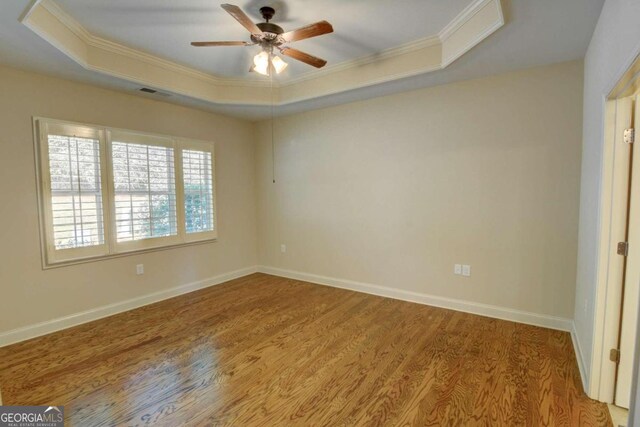 empty room featuring light hardwood / wood-style floors, a raised ceiling, crown molding, and ceiling fan