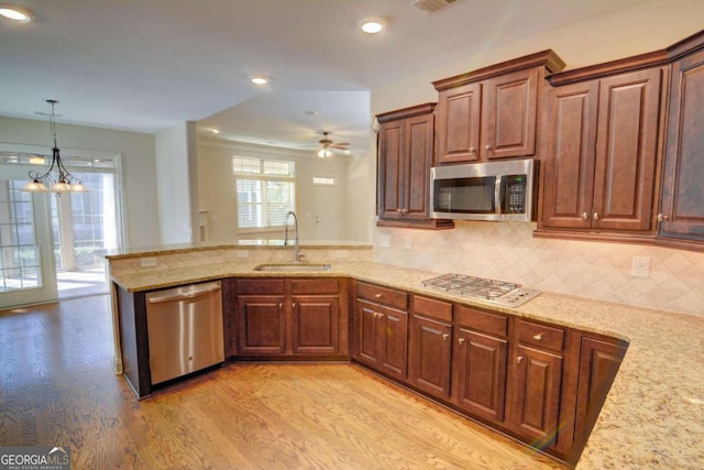 kitchen featuring light hardwood / wood-style floors, stainless steel appliances, backsplash, sink, and ceiling fan with notable chandelier