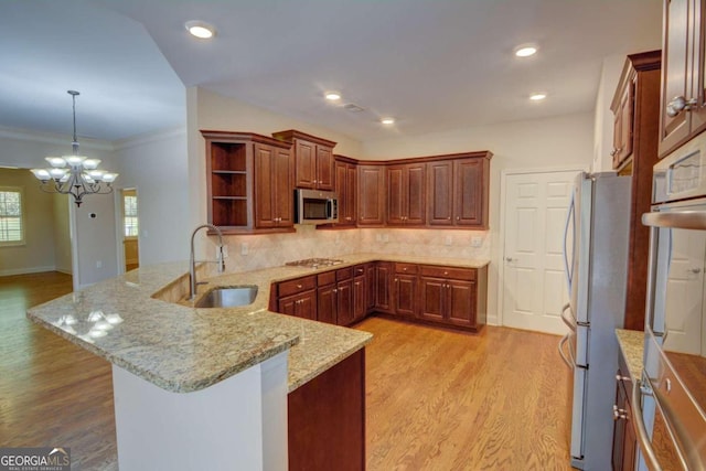 kitchen with light stone counters, light wood-type flooring, sink, and kitchen peninsula