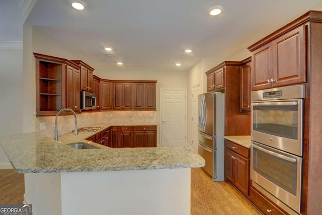 kitchen with sink, appliances with stainless steel finishes, kitchen peninsula, and light hardwood / wood-style floors