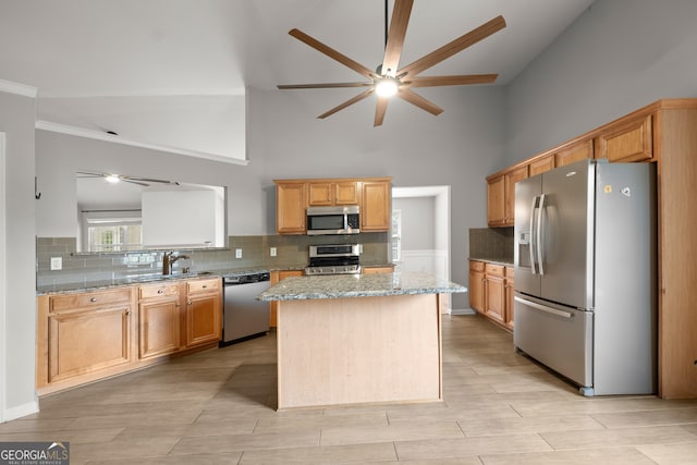 kitchen with light stone counters, a kitchen island, sink, a towering ceiling, and stainless steel appliances