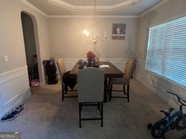 unfurnished dining area featuring a tray ceiling, ornamental molding, carpet flooring, and an inviting chandelier