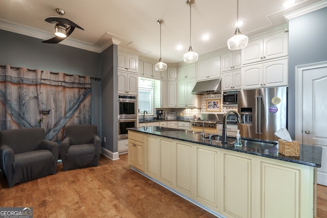 kitchen with appliances with stainless steel finishes, an island with sink, backsplash, dark stone counters, and pendant lighting