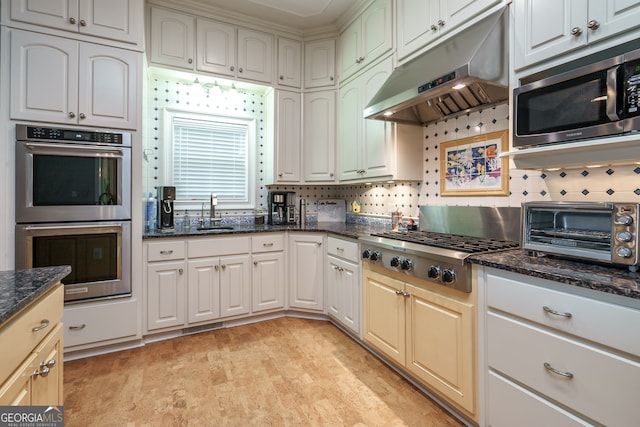 kitchen with decorative backsplash, appliances with stainless steel finishes, dark stone countertops, light hardwood / wood-style floors, and sink