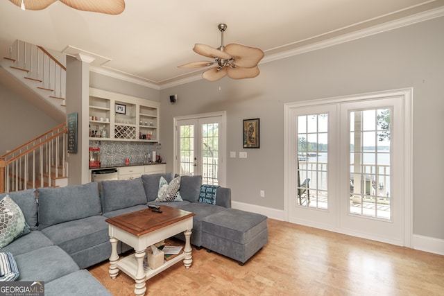 living room featuring light wood-type flooring, french doors, ceiling fan, bar, and ornamental molding