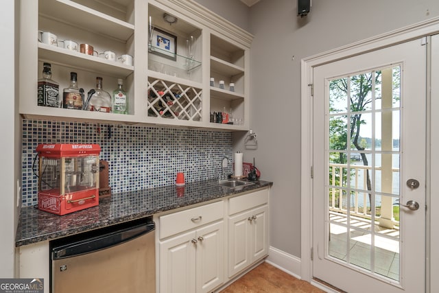 bar with decorative backsplash, white cabinets, stainless steel dishwasher, dark stone countertops, and sink