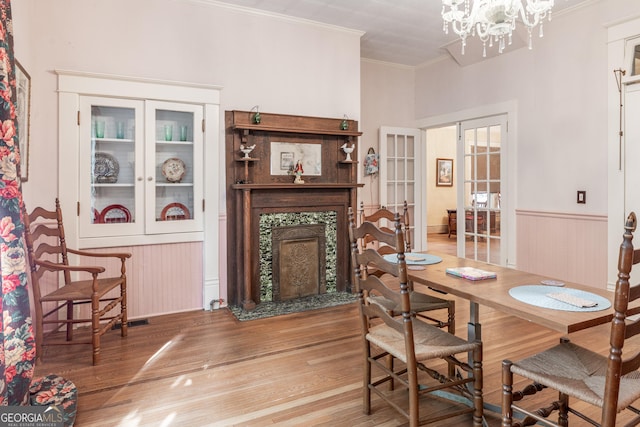 dining space with a notable chandelier, a premium fireplace, crown molding, hardwood / wood-style flooring, and french doors