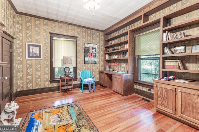 office with built in features, crown molding, built in desk, and light wood-type flooring