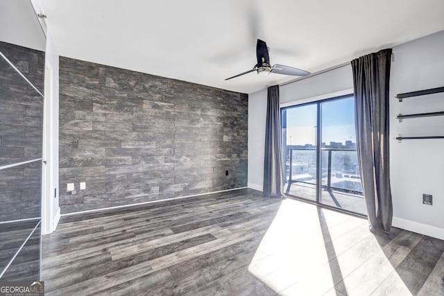 empty room featuring dark wood-type flooring, ceiling fan, and tile walls