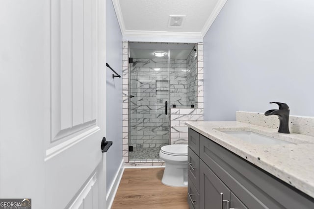 bathroom with a shower with door, hardwood / wood-style flooring, toilet, ornamental molding, and vanity