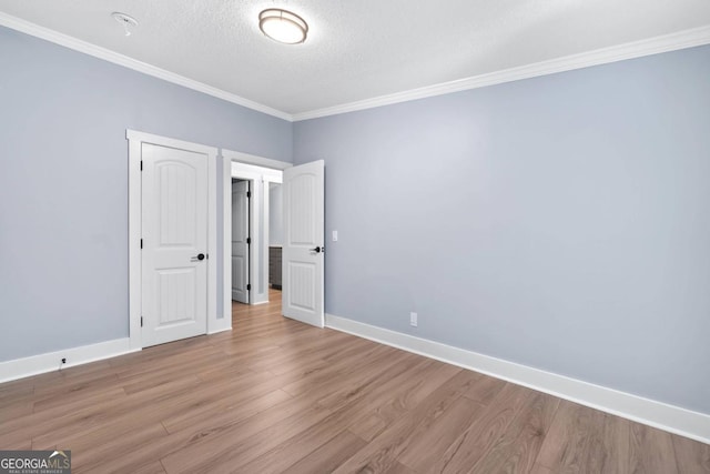 empty room featuring crown molding, a textured ceiling, and light wood-type flooring