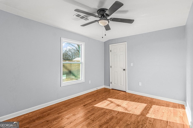 spare room with a ceiling fan, visible vents, wood finished floors, and baseboards