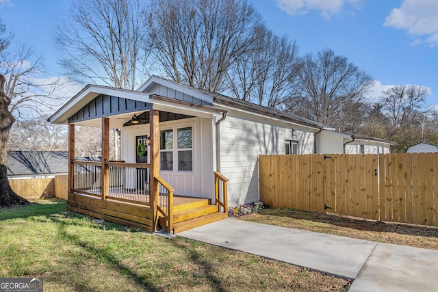 exterior space with a front yard, fence, board and batten siding, and ceiling fan