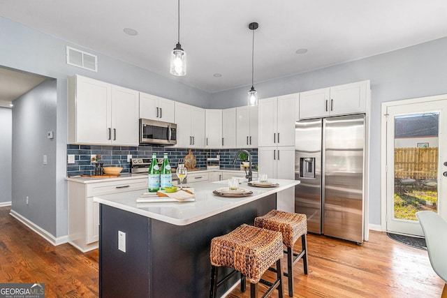 kitchen with visible vents, backsplash, white cabinetry, stainless steel appliances, and light countertops