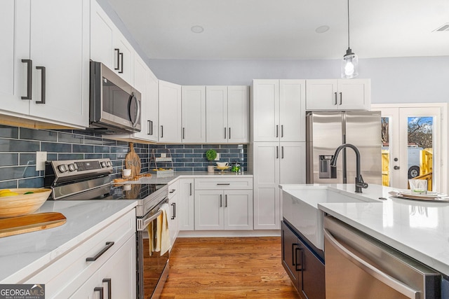 kitchen with tasteful backsplash, appliances with stainless steel finishes, light wood-style floors, hanging light fixtures, and white cabinetry