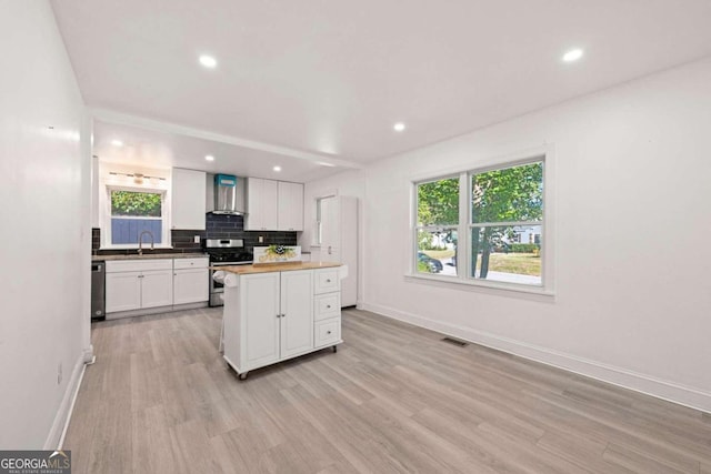 kitchen featuring wall chimney range hood, white cabinets, appliances with stainless steel finishes, light hardwood / wood-style flooring, and butcher block counters