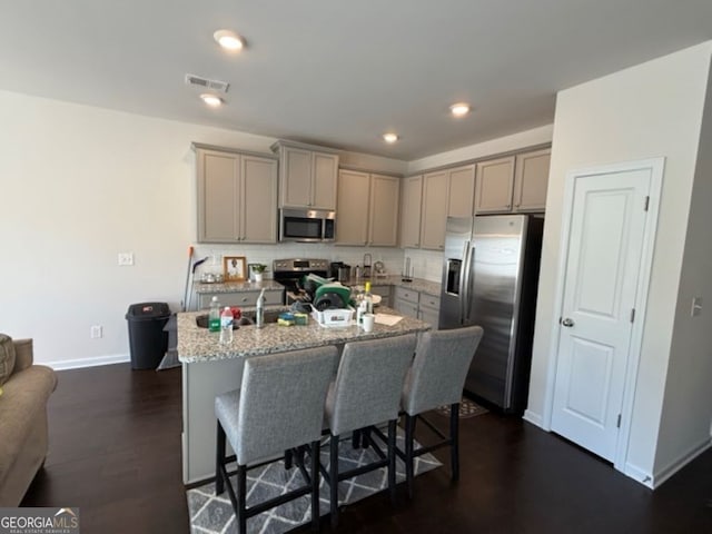 kitchen featuring appliances with stainless steel finishes, light stone countertops, dark hardwood / wood-style floors, a kitchen island with sink, and gray cabinets