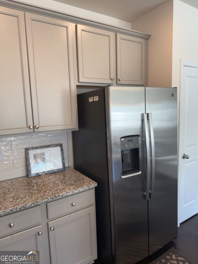 kitchen featuring light stone counters, tasteful backsplash, gray cabinets, dark hardwood / wood-style floors, and stainless steel fridge