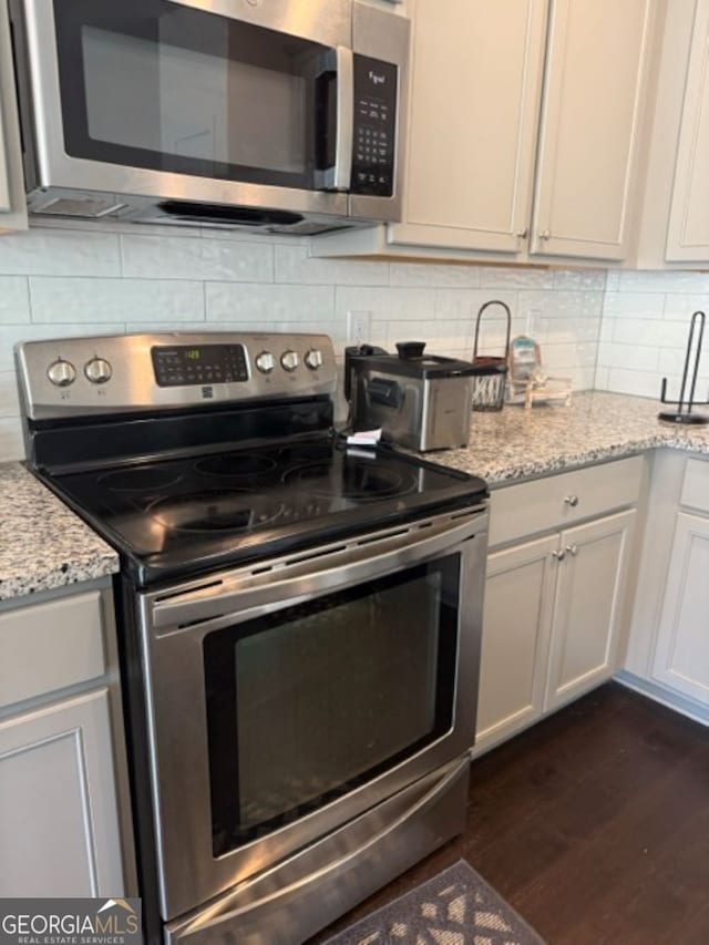 kitchen featuring stainless steel appliances, white cabinetry, light stone countertops, decorative backsplash, and dark wood-type flooring