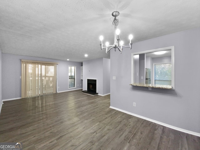 unfurnished living room featuring a textured ceiling, a notable chandelier, dark hardwood / wood-style floors, and plenty of natural light