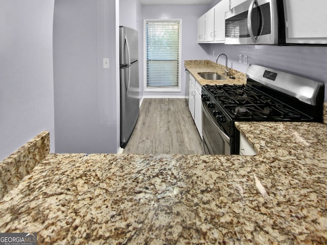 kitchen with appliances with stainless steel finishes, light hardwood / wood-style flooring, white cabinets, and sink