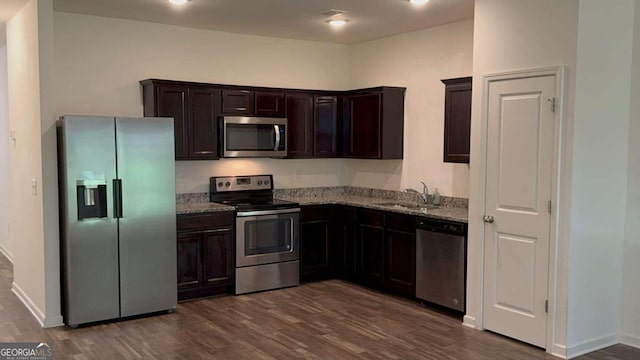 kitchen with appliances with stainless steel finishes, light stone countertops, dark wood-type flooring, dark brown cabinetry, and sink