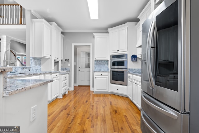 kitchen featuring tasteful backsplash, appliances with stainless steel finishes, white cabinetry, light wood-type flooring, and ornamental molding