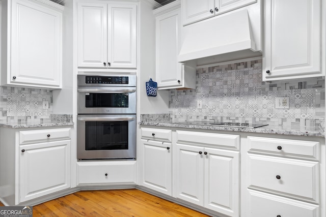 kitchen featuring premium range hood, white cabinetry, light hardwood / wood-style flooring, black electric stovetop, and stainless steel double oven