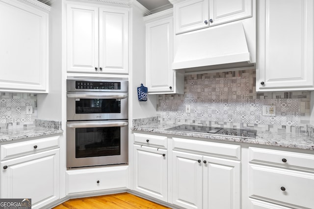 kitchen with stainless steel double oven, black electric cooktop, light hardwood / wood-style flooring, white cabinets, and premium range hood