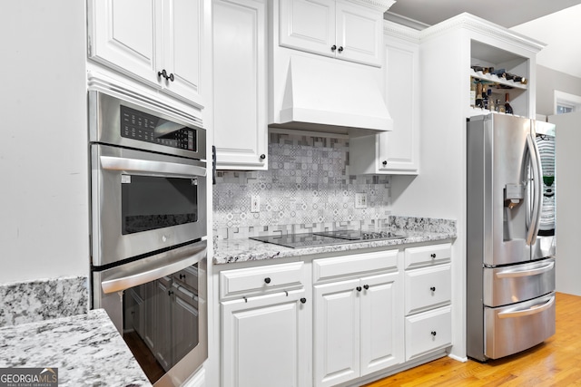 kitchen with custom range hood, light stone countertops, white cabinets, light wood-type flooring, and appliances with stainless steel finishes