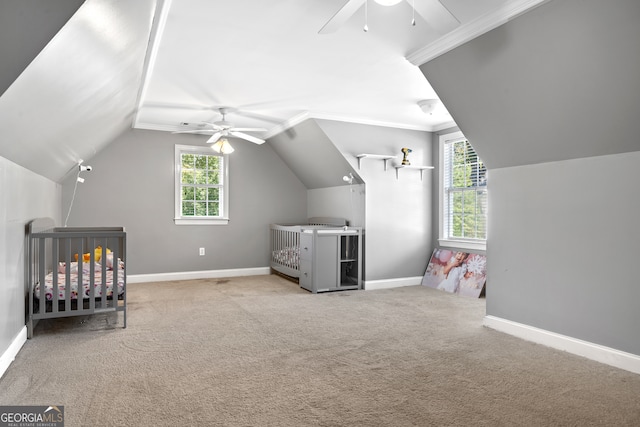 unfurnished bedroom featuring lofted ceiling, a crib, light carpet, crown molding, and ceiling fan