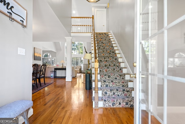 staircase featuring decorative columns, hardwood / wood-style flooring, and a towering ceiling