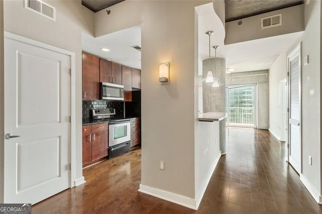 kitchen featuring dark wood-type flooring, backsplash, appliances with stainless steel finishes, and hanging light fixtures