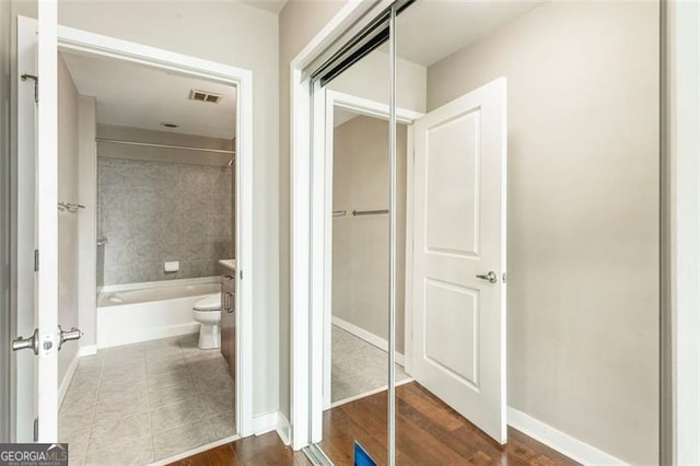 bathroom with toilet, tiled shower / bath combo, and wood-type flooring