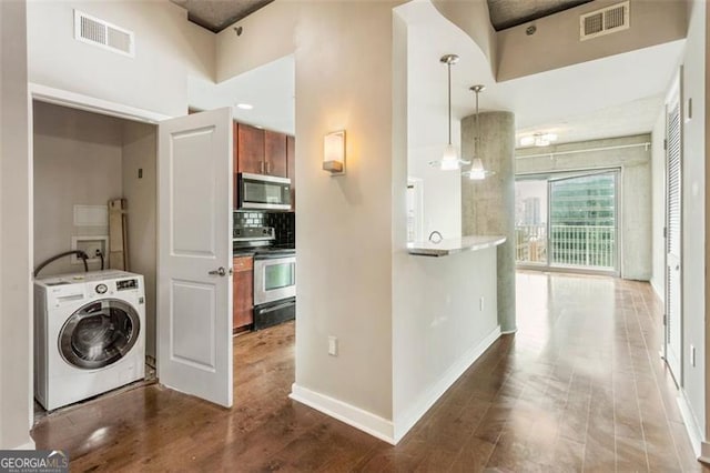 kitchen featuring washer / clothes dryer, kitchen peninsula, stainless steel appliances, hardwood / wood-style floors, and a towering ceiling