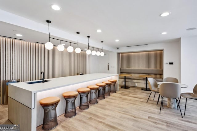 bar with light hardwood / wood-style floors, decorative light fixtures, and sink